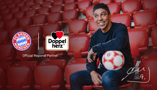 A man sits in a stadium seat holding a soccer ball, smiling at the camera. Logos for FC Bayern München and Doppelherz are displayed nearby, with the text "Official Regional Partner" underneath. The background features empty red stadium seats.
